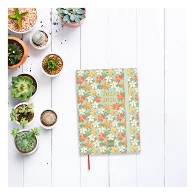 Caderno com capa floral e anos 2023 2024 ao centro, junto a vasos com suculentas sobre mesa branca