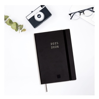 Agenda preta 2025 2026 com câmara fotográfica, óculos e folhas verdes