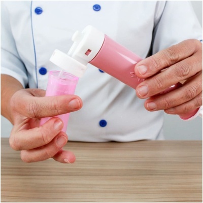 Duas mãos segurando embalagem plástica rosa com tampa branca sobre mesa de madeira