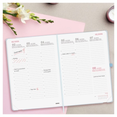 Agenda aberta com texto e anotações sobre mesa com flores e vela