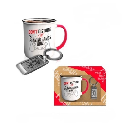 Conjunto de caneca branca com pega vermelha e porta-chaves metálico com desenho de comando de videojogos e embalagem em cartão.