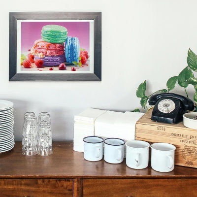 Quadro colorido de macarons em cima de móvel de madeira com canecas brancas e telefone preto