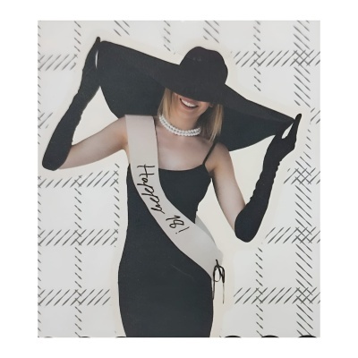 Mulher vestida de preto com faixa 'HAPPY 18!' e chapéu largo preto