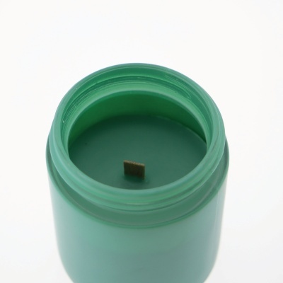 Vela verde num frasco de vidro com pavio quadrado de madeira.