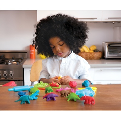 Criança a brincar com brinquedos de dinossauros coloridos numa cozinha