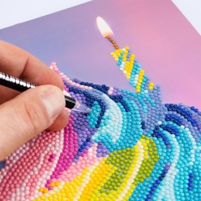 Mosaico colorido com mão a colocar peças numa tela rosa e roxa.