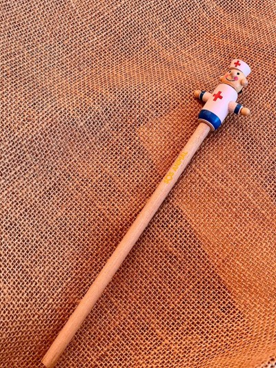 Lápis de madeira com figura de enfermeira no topo sobre superfície de juta