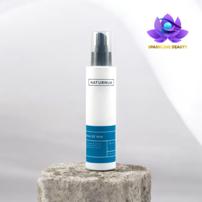 Frasco branco com dispensador preto e etiqueta azul em base de pedra cinzenta.