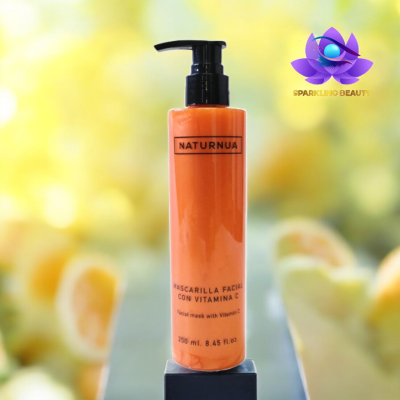 Frasco de máscara facial laranja com doseador preto, texto em espanhol, fundo com frutas cítricas