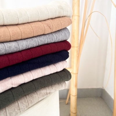 Suéteres de malha dobrados em várias cores empilhados num canto interior com piso de cerâmica e bambu.