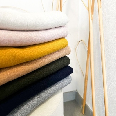 Pilhas de tecidos ou roupas coloridas dobradas numa superfície branca junto a parede e ramos secos