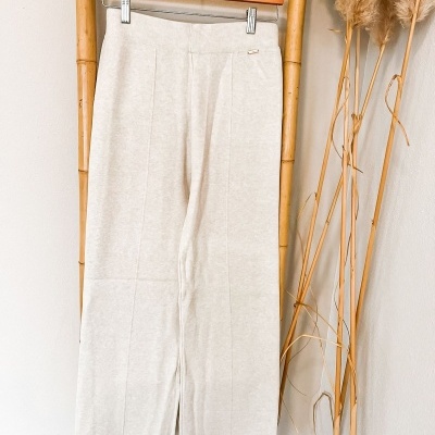 Calças compridas creme penduradas em cabide de madeira numa estrutura de bambu