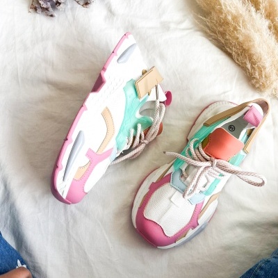 Par de sapatilhas desportivas coloridas sobre tecido branco com flores secas e penas ao lado