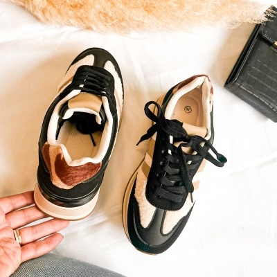 Par de sapatilhas bege, preto e branco com padrão pelo e saco preto ao lado.