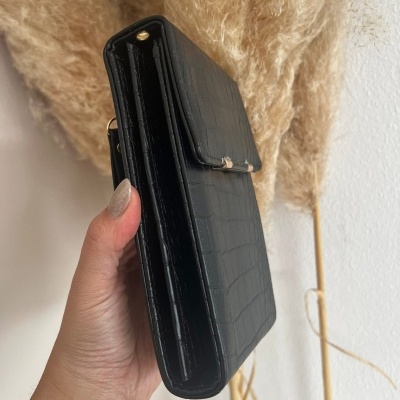 Carteira preta com padrão de crocodilo e detalhes dourados sendo segurada por uma mão.