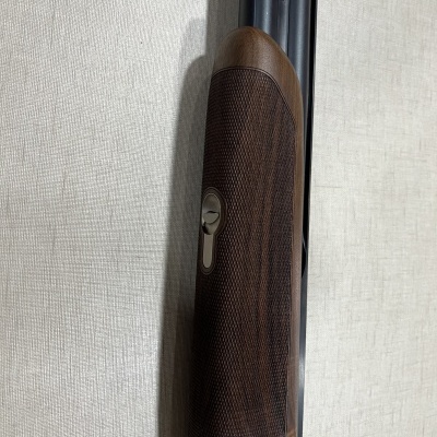 Arma de caça com guarda-mão em madeira escura trabalhada e canos metálicos pretos