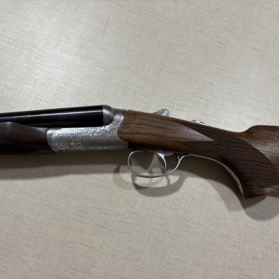 Espingarda Beretta com madeira castanha e metal prateado gravado em fundo claro