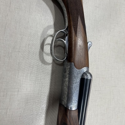 Espingarda de caça com armação em madeira e metal gravado sobre superfície clara