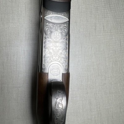 Espingarda com acabamento em metal gravado e madeira escura sobre fundo cinzento