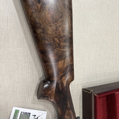 Coronha de arma de fogo em madeira castanha com padrão marmorizado ao lado de uma etiqueta e estojo vermelho