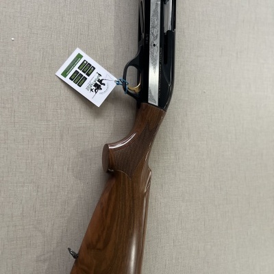 Espingarda com coronha em madeira e metal com etiqueta pendurada sobre tecido bege.