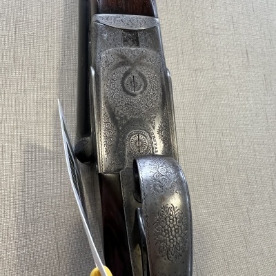 Espingarda com gravações metálicas e cabo em madeira sobre tecido bege.