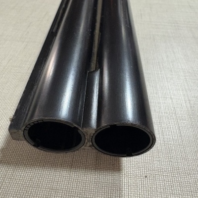 Extremidade de cano duplo metálico preto fosco sobre superfície cinzenta texturizada