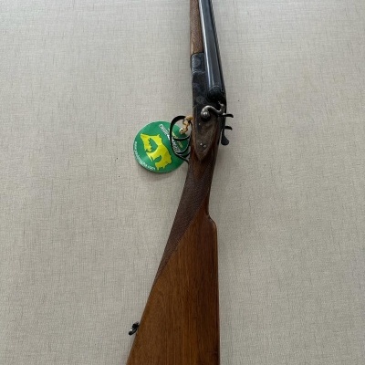 Espingarda de canos duplos com coronha de madeira castanha e canos pretos com etiqueta verde e amarela