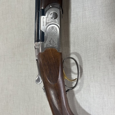 Espingarda Beretta com madeira castanha e detalhes metálicos prateados sobre superfície bege