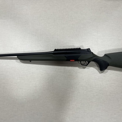 Espingarda preta e cinzenta com empunhadura texturizada encostada numa parede branca