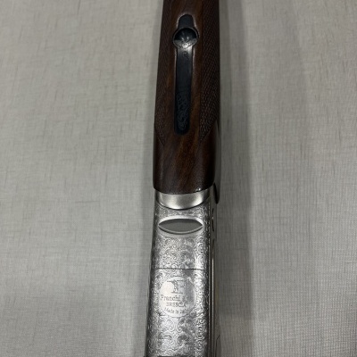 Arma de fogo com madeira escura e metal gravado sobre tecido cinzento claro