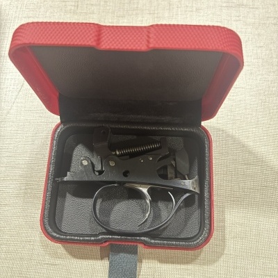 Mecanismo de gatilho metálico preto em estojo vermelho aberto sobre tecido bege