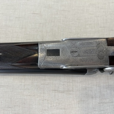 Parte superior de espingarda com madeira escura e metal gravado em fundo bege