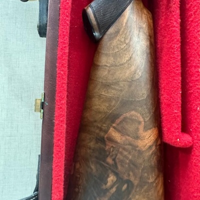 Coronha de espingarda em madeira castanho escuro em mala vermelha.