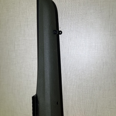 Rifle com coronha verde escura texturizada encostado a uma parede branca