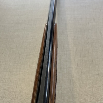 Espingarda cano duplo preto e coronha madeira castanha em superfície bege