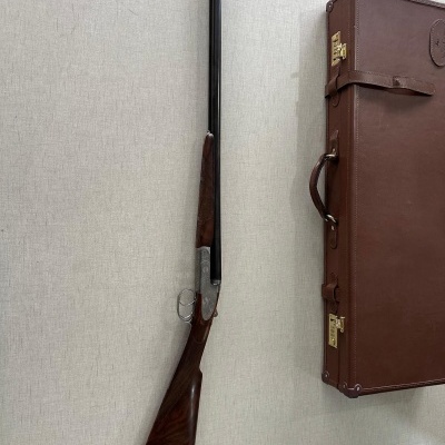 Espingarda de canos duplos com coronha de madeira escura e mala castanha de transporte