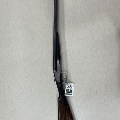 Espingarda de canos duplos com coronha de madeira escura e metal prateado pendurada na parede