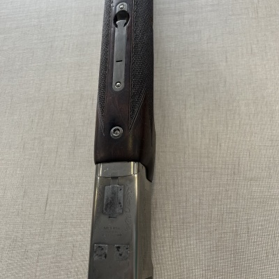 Espingarda de madeira escura e metal prateado sobre tecido cinzento.