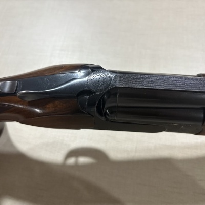 Espingarda de canos duplos com cabo em madeira e metal preto com gravação circular.