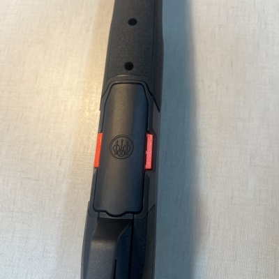 Peça preta de arma com logotipo BERETTA sobre superfície clara