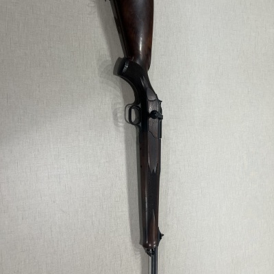 Rifle com coronha em madeira escura e cano metálico preto sobre fundo claro