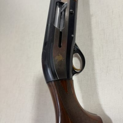 Arma de caça com coronha em madeira e caixa de mecanismos preta com detalhe de pássaro dourado