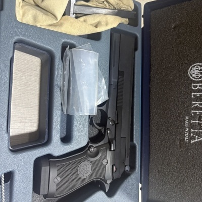 Pistola preta Beretta numa caixa azul com acessórios