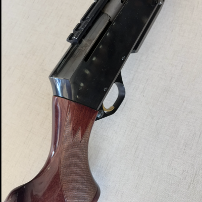 Arma de fogo com cabo de madeira e corpo metálico preto sobre fundo claro