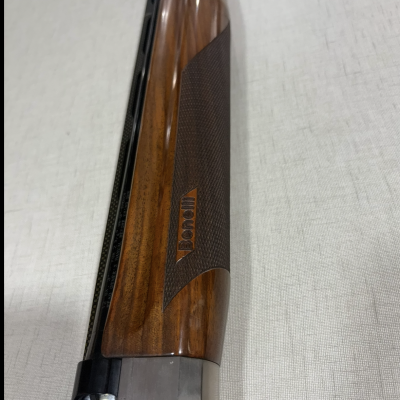Espingarda com madeira castanha e detalhes escuros texturizados, marca Benelli visível