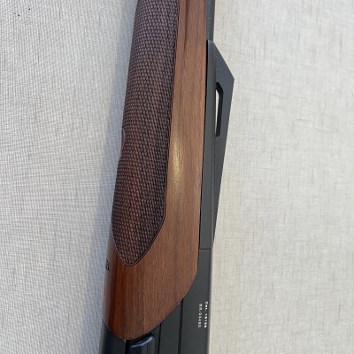 Espingarda com coronha de madeira castanha e corpo metálico preto sobre tecido claro.