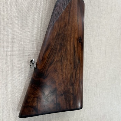 Coronha de arma de fogo em madeira castanho escuro com textura quadriculada e fixador metálico