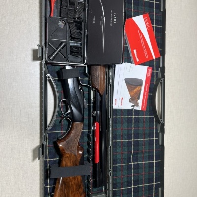 Estojo aberto com caçadeira desmontada, ferramentas e manuais