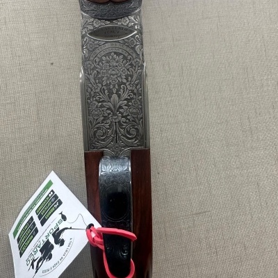 Espingarda com madeira castanha e detalhes metálicos gravados com padrão floral, etiqueta branca com texto e cordão vermelho.